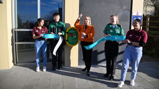 Vice-Chancellor Professor Evelyn Welch and four medical students Aashna Bali, Abbi Bow, Jason Leung and Victoria Belsten. Evelyn is cutting a ribbon in front of a new wall-mounted defibrillator.